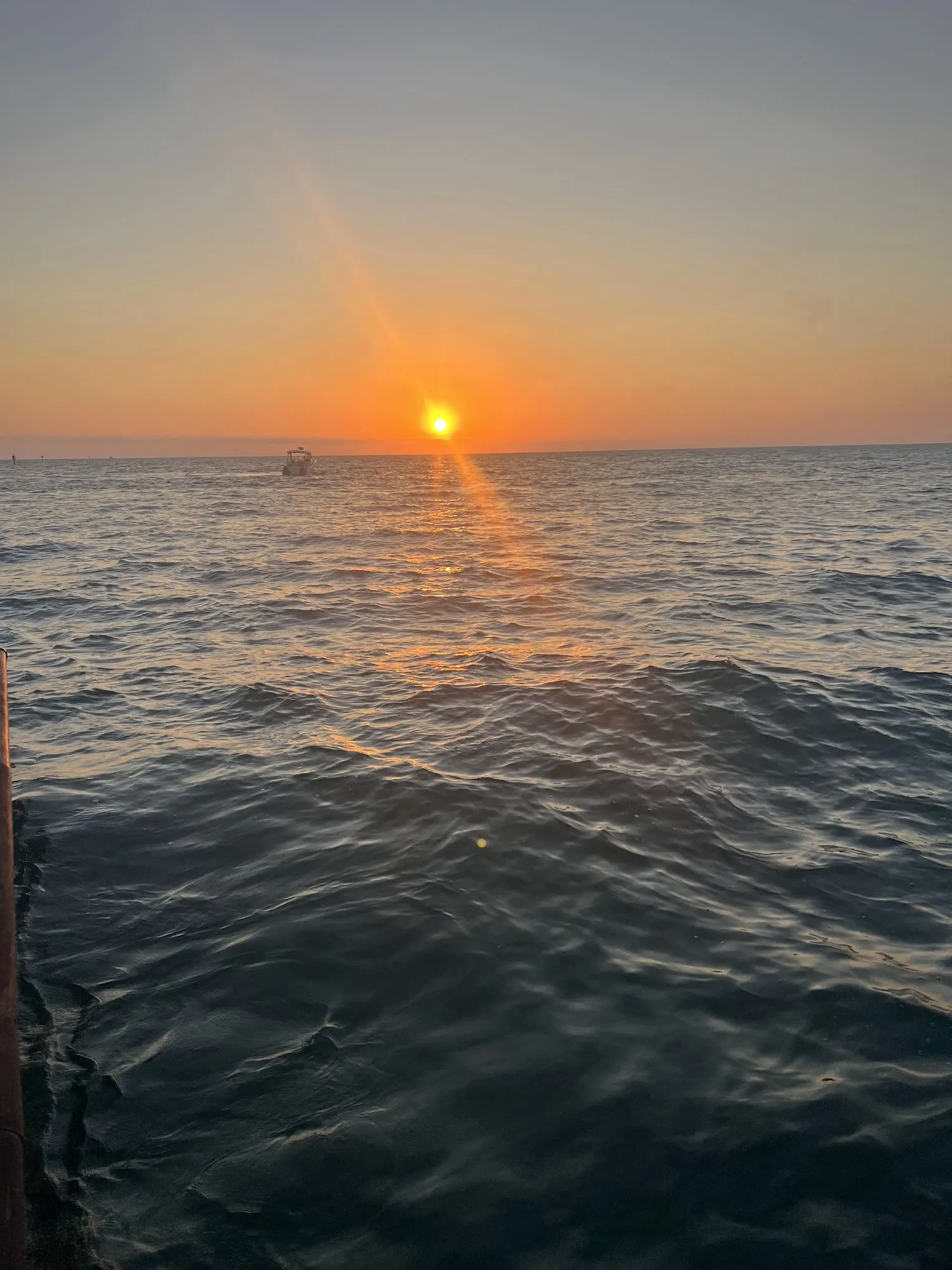 Sun bursting low over the Gulf at sunset with a boat on the horizon