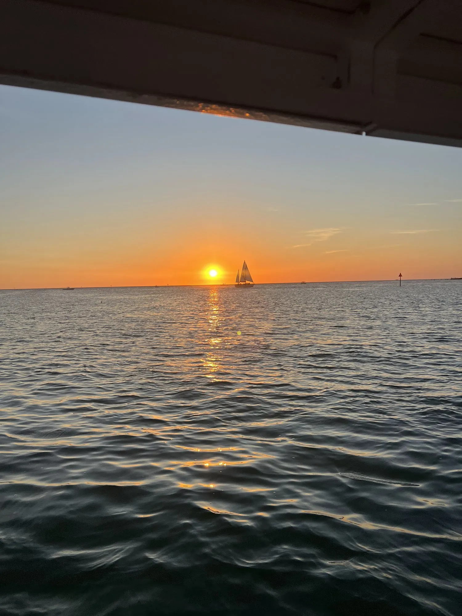 Sailboat silhouetted against an orange sunset, seen from Phat Kat's deck